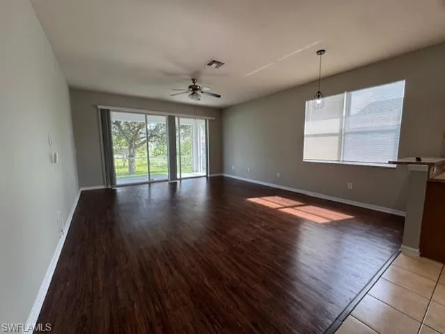 Empty room featuring healthy amount of natural light, ceiling fan, and dark wood-style flooring
