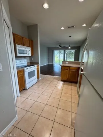 Kitchen featuring white appliances, brown cabinetry, hanging light fixtures, light tile patterned floors, and recessed lighting