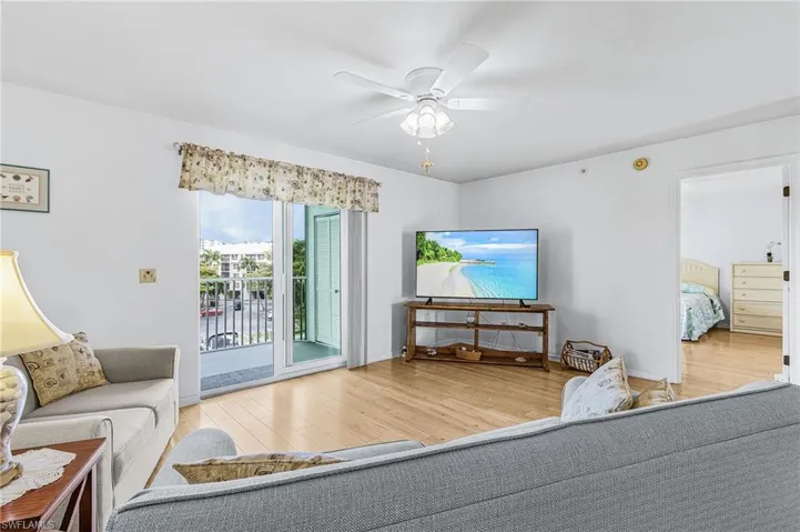 Living area featuring wood-finish flooring, white walls, and a white ceiling fan with integrated lighting