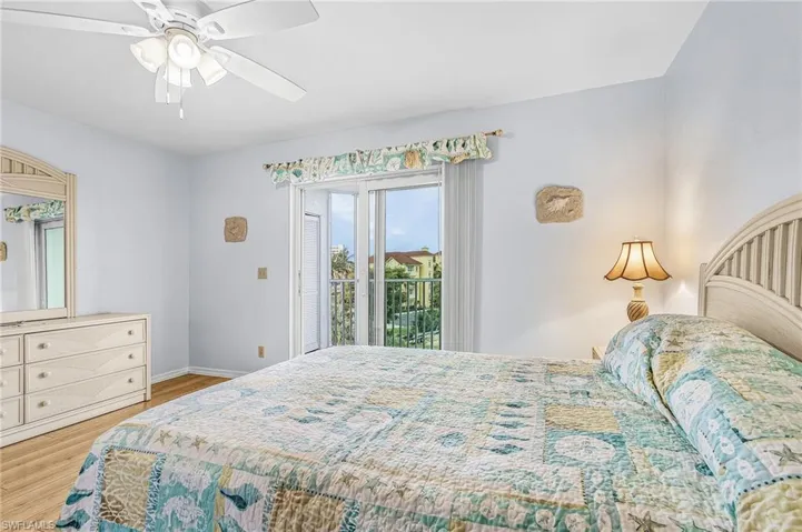 Bedroom featuring sliding glass doors opening to a balcony, wood-finish flooring, a ceiling fan with integrated lighting, and white painted walls