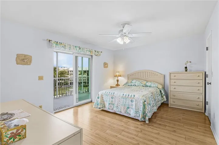 Sliding glass doors opening to an exterior balcony, wood-finish flooring, white walls, and a ceiling fan with integrated lighting