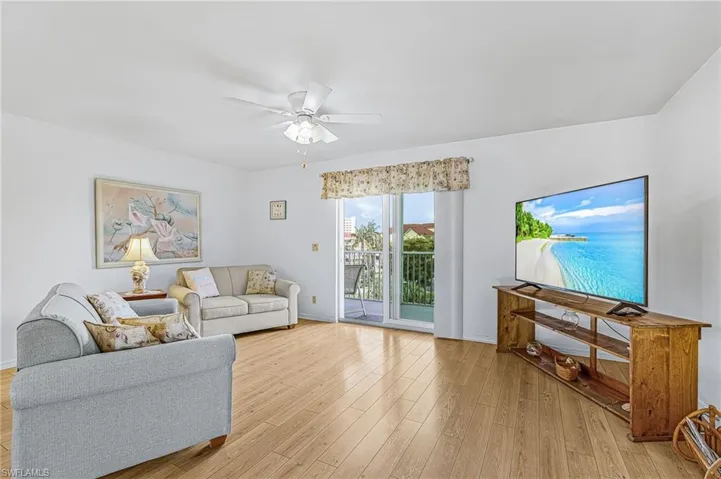 Bright living area featuring wood-finish flooring, a ceiling fan with integrated lighting, and a sliding glass door leading to an outdoor balcony