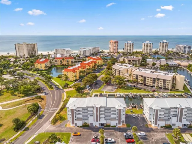 Coastal community with multi-story buildings, marina access, and proximity to a sandy beach and open water
