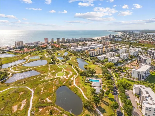 Expansive coastal landscape featuring a broad sandy beach, numerous high-rise buildings, multiple golf course fairways, several water features, and a community swimming pool