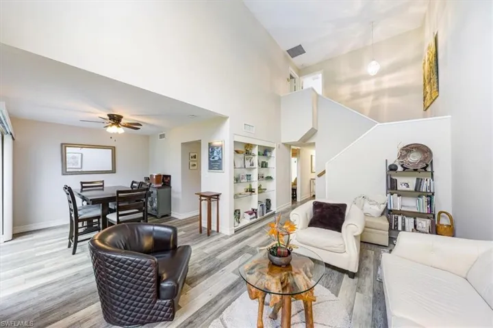 Living room with light wood-style floors, a towering ceiling, built in shelves, a ceiling fan, and stairs