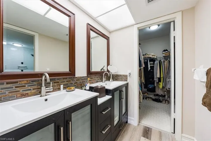 Full bath featuring vanity, wood finished floors, a walk in closet, tasteful backsplash, and a tile shower