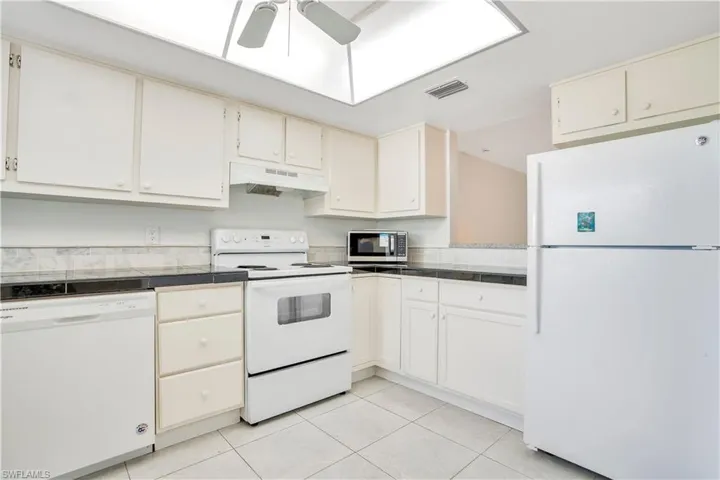 Kitchen with white appliances, ceiling fan, light tile patterned flooring, cream cabinetry, and tile countertops