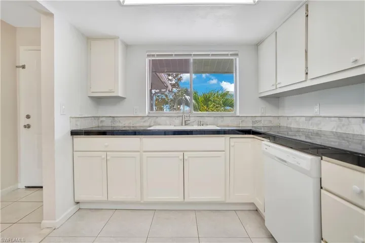 Kitchen with dishwasher, white cabinets, light tile patterned floors, and tile countertops