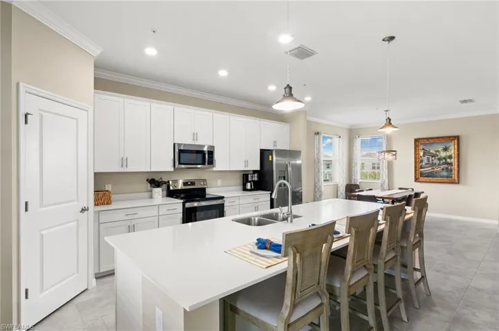 Kitchen featuring an expansive center island with an integrated sink, stainless steel appliances, white cabinetry, and light-toned flooring