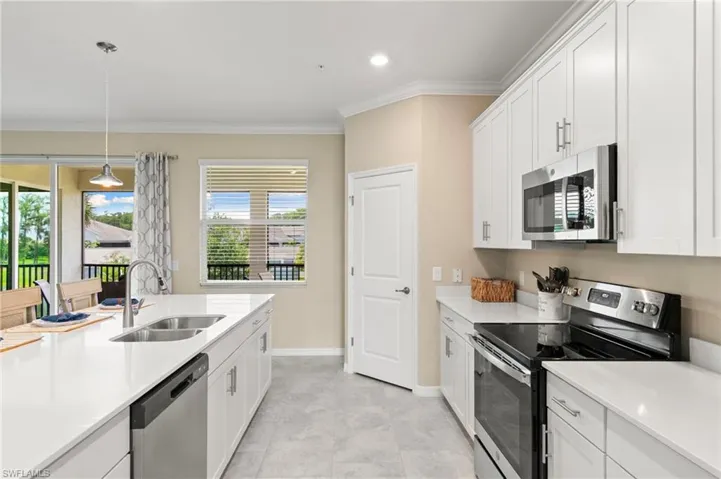 Modern kitchen featuring white cabinetry, light-colored countertops, stainless steel appliances, and a central island with an undermount sink