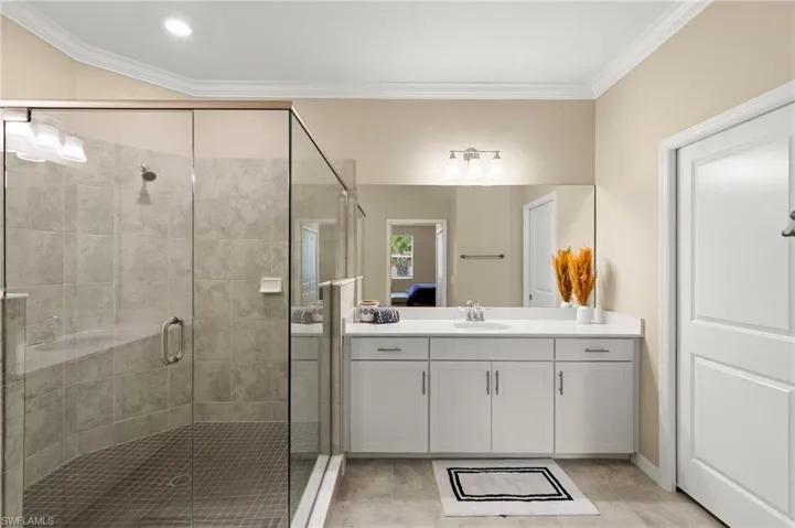 Spacious bathroom featuring a glass-enclosed shower with tile surround and integrated bench, a long vanity with dual sinks, white cabinetry, and a large mirror, complemented by tile flooring and a neutral color palette