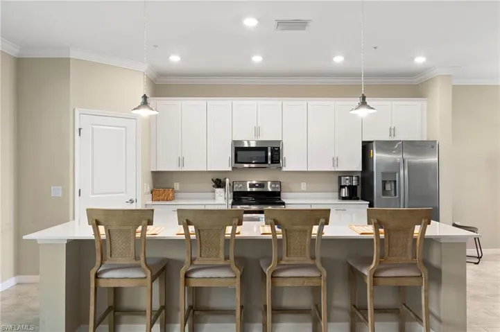 Bright kitchen featuring white shaker cabinetry, stainless steel appliances, a white countertop island with seating, recessed lighting, and pendant lighting fixtures