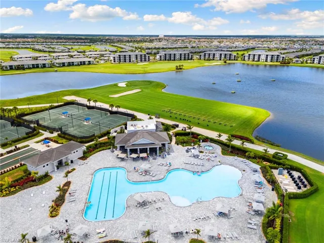 Expansive aerial showcasing a large resort-style pool area, multiple tennis courts, and a golf course bordering a significant body of water