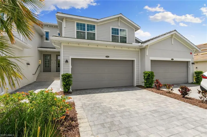 Contemporary two-story exterior featuring a light gray and white facade, dual garage doors, and a paver driveway