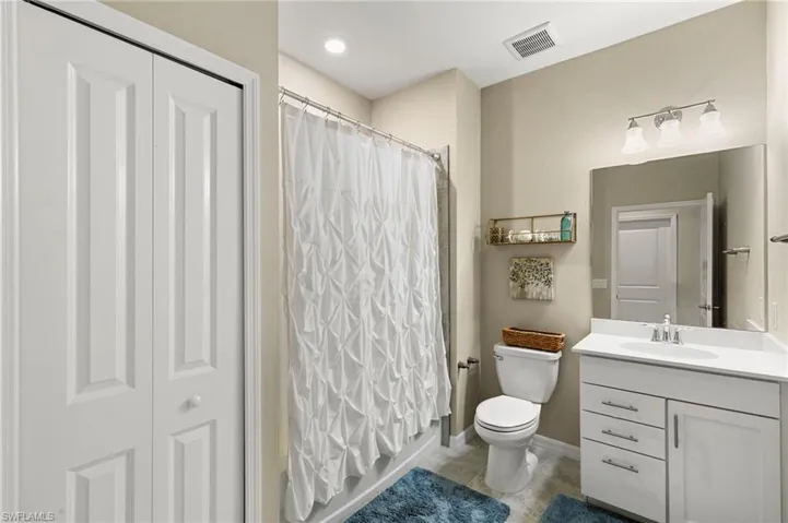 Bathroom featuring a single vanity with white cabinetry, a built-in toilet, a shower with a shower curtain, a large mirror, and recessed lighting