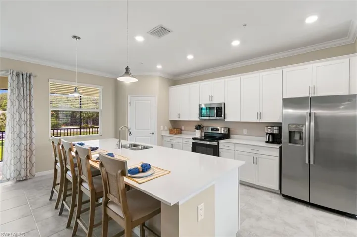 Modern kitchen featuring an expansive island with seating for four, white shaker-style cabinetry, stainless steel appliances, a stainless steel sink with a gooseneck faucet, and recessed lighting
