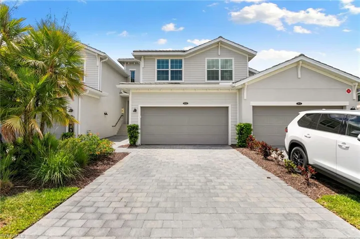 Contemporary townhome exterior featuring light-toned siding and stucco, a paver driveway, and an integrated garage