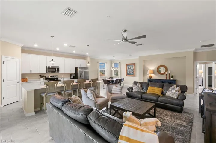 Open-concept living space featuring light tile flooring, a contemporary ceiling fan, recessed lighting, a kitchen island with pendant lighting, and white cabinetry with stainless steel appliances