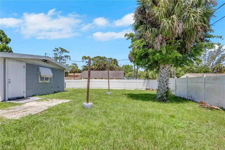 Expansive grassy yard with a mature palm tree and white perimeter fencing