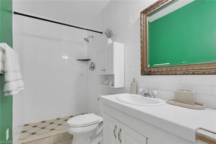 Bathroom featuring a white tile shower with a patterned floor, white vanity with integrated sink, chrome fixtures, and a decorative framed mirror