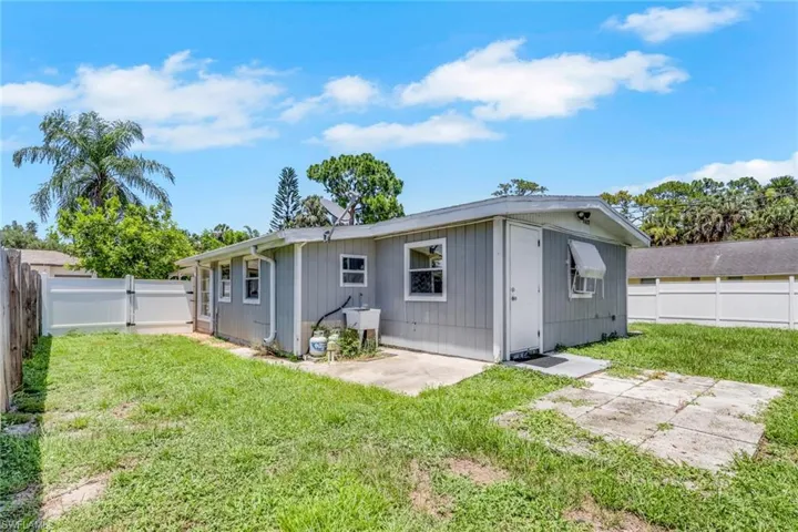 Expansive backyard featuring a white vinyl privacy fence, concrete patio areas, and a rear structure with horizontal siding