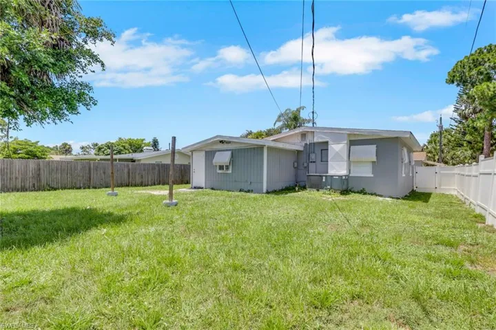 Expansive grassy backyard featuring a wood privacy fence, white vinyl fencing, mature trees, and a single-story residence with a light gray exterior