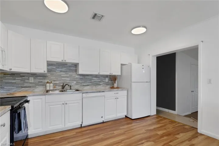 Bright kitchen featuring white cabinetry, a mosaic tile backsplash, light-toned countertops, wood-finish flooring, and a white appliance suite