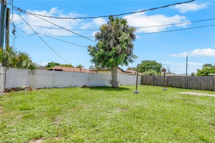 Spacious green yard featuring a mature palm tree, white privacy fencing, and wood fencing