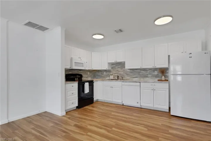 White kitchen cabinetry with silver hardware and a light-toned wood-finish flooring