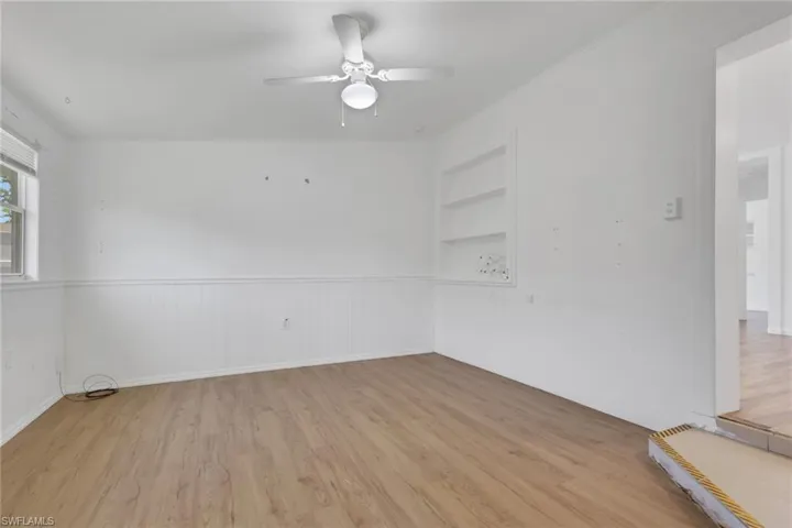 Room featuring wood-finish flooring, white wainscoting, a ceiling fan with integrated lighting, a built-in wall niche, and an exterior-facing window