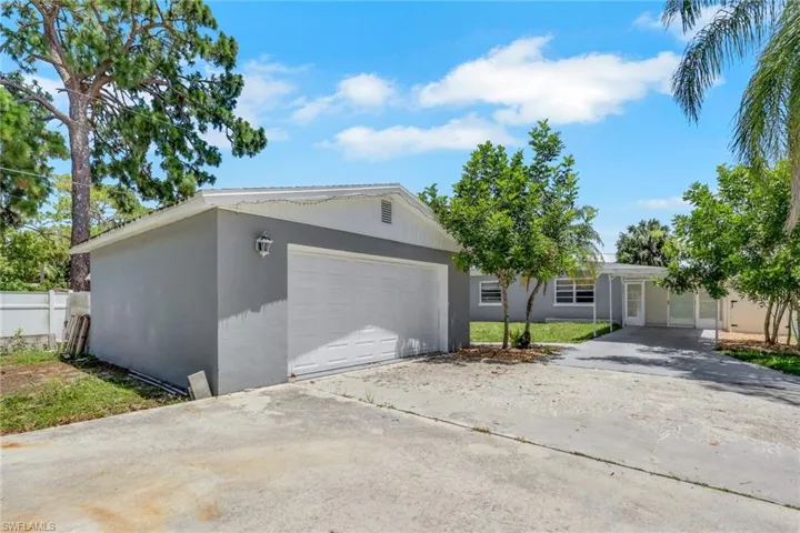 Spacious concrete driveway featuring a two-car garage with a white sectional door, a light gray stucco exterior, and mature landscaping