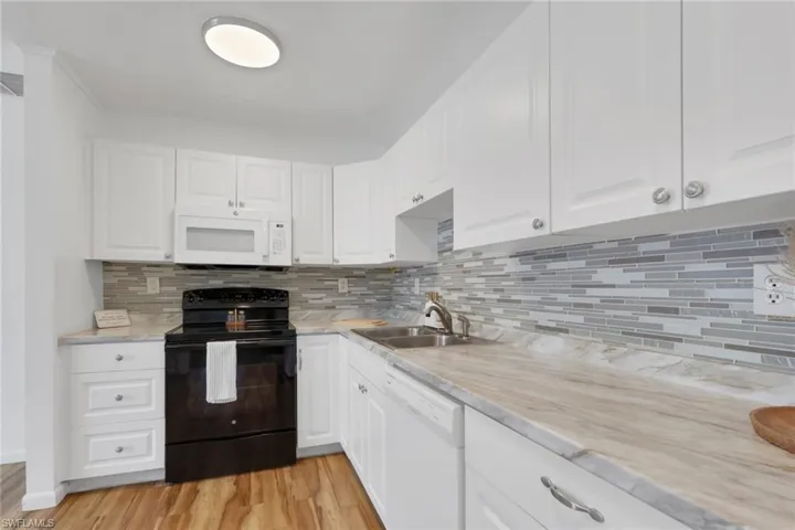 Kitchen featuring white cabinetry, a black range with an overhead microwave, and wood-finish flooring