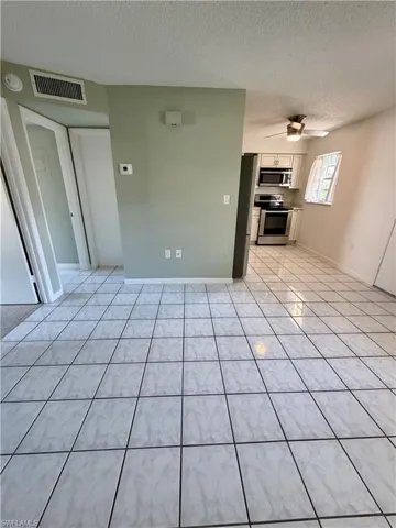 Unfurnished living room featuring a textured ceiling, light tile patterned floors, and a ceiling fan