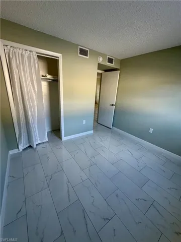 Unfurnished bedroom featuring light marble finish floors, a textured ceiling, and a closet