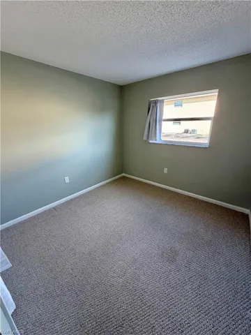Carpeted empty room with a textured ceiling and baseboards
