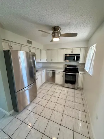 Kitchen with appliances with stainless steel finishes, a textured ceiling, white cabinetry, a ceiling fan, and light tile patterned flooring