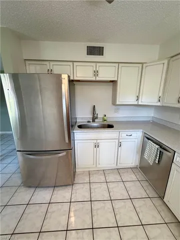 Kitchen featuring stainless steel appliances, white cabinets, a textured ceiling, light tile patterned flooring, and light stone countertops