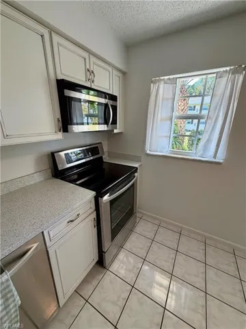 Kitchen with appliances with stainless steel finishes, a textured ceiling, white cabinets, light stone countertops, and light tile patterned flooring