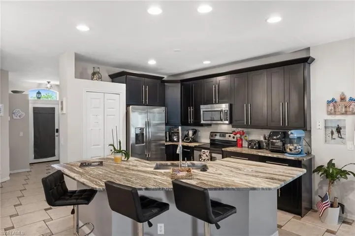 Kitchen featuring appliances with stainless steel finishes, a kitchen bar, light stone countertops, backsplash, and recessed lighting