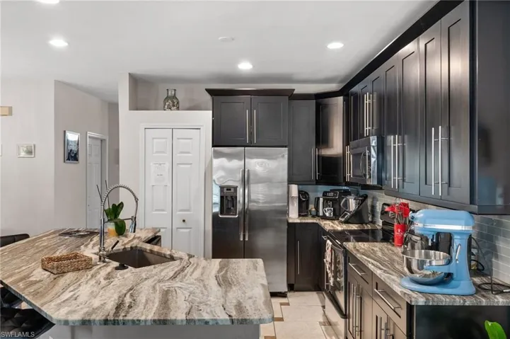 Kitchen featuring appliances with stainless steel finishes, a sink, light stone countertops, decorative backsplash, and a kitchen island with sink