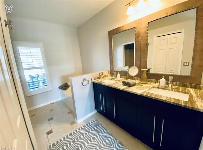 Full bathroom with double vanity, a bath, baseboards, and tile patterned floors