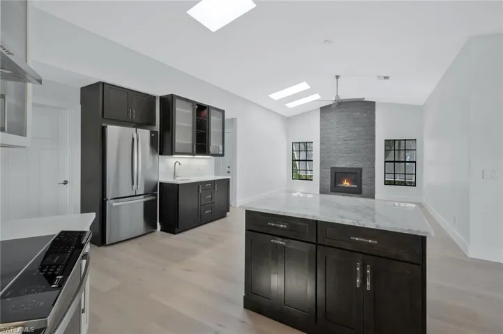 Kitchen with light wood-style flooring, vaulted ceiling with skylight, appliances with stainless steel finishes, glass insert cabinets, and a sink