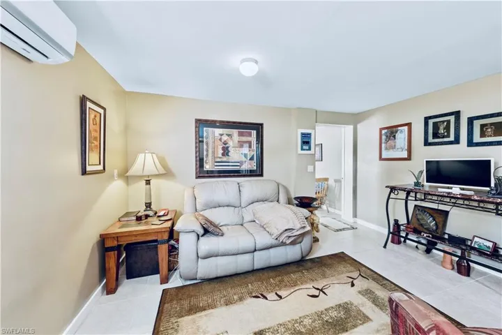 Tiled living room with an AC wall unit and baseboards