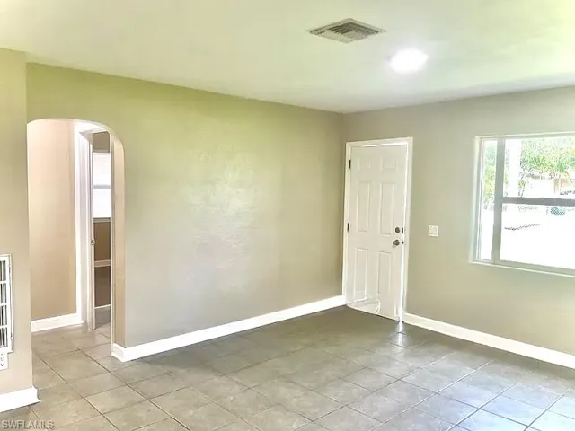 Tiled empty room featuring visible vents, arched walkways, and baseboards