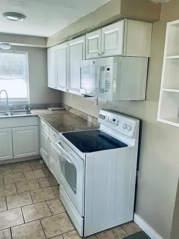 Kitchen with light tile patterned flooring, white appliances, white cabinetry, and a sink