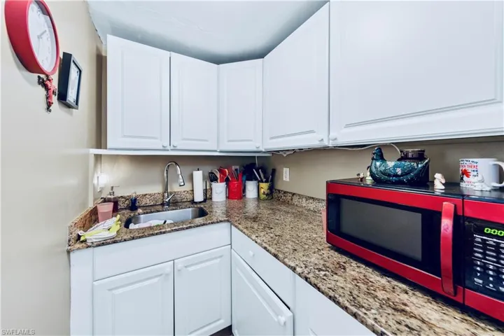 Kitchen with light stone counters, white cabinetry, and a sink