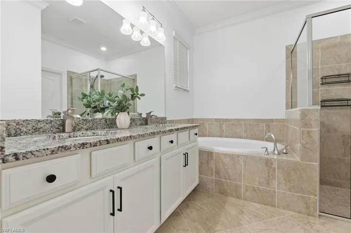 Full bath featuring a shower stall, ornamental molding, a garden tub, and double vanity