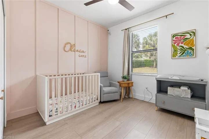Bedroom with a crib, light wood-style floors, and a ceiling fan