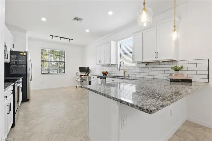 Kitchen featuring a peninsula, crown molding, an office area, dark stone countertops, and white cabinetry