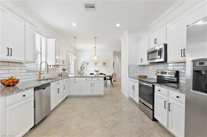 Kitchen with stainless steel appliances, white cabinets, light stone counters, hanging light fixtures, and ornamental molding